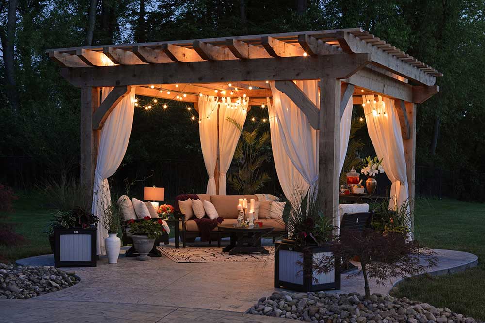 A stone patio with a gazebo illuminated by string lights