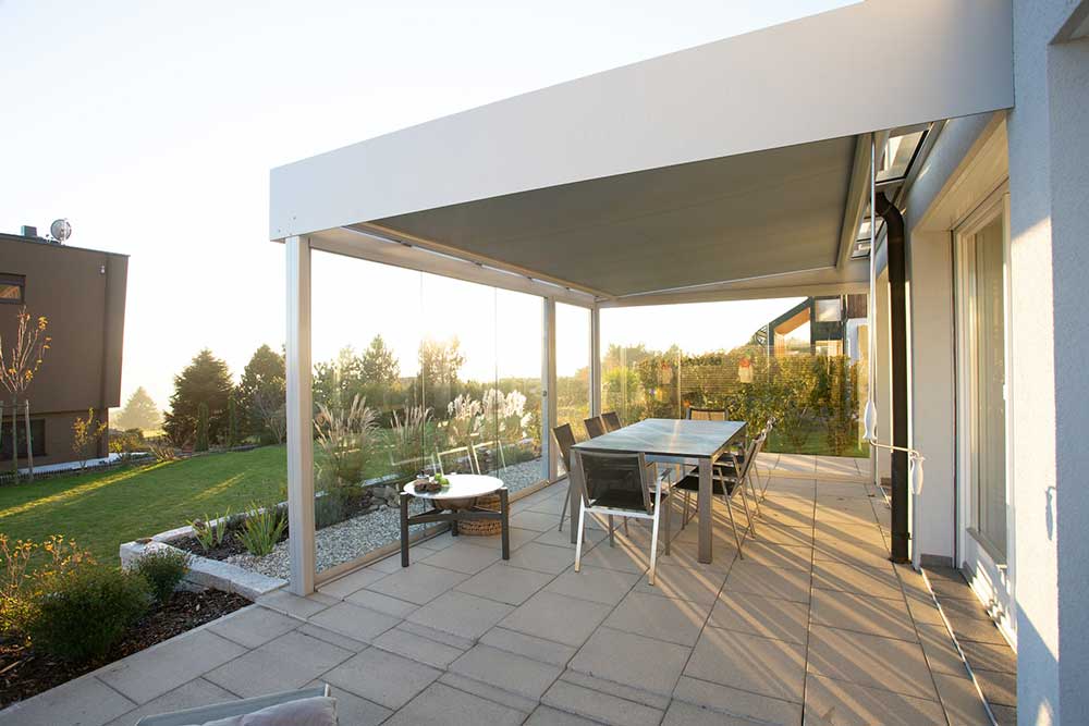 A white patio made of stone with an awning and a dining table