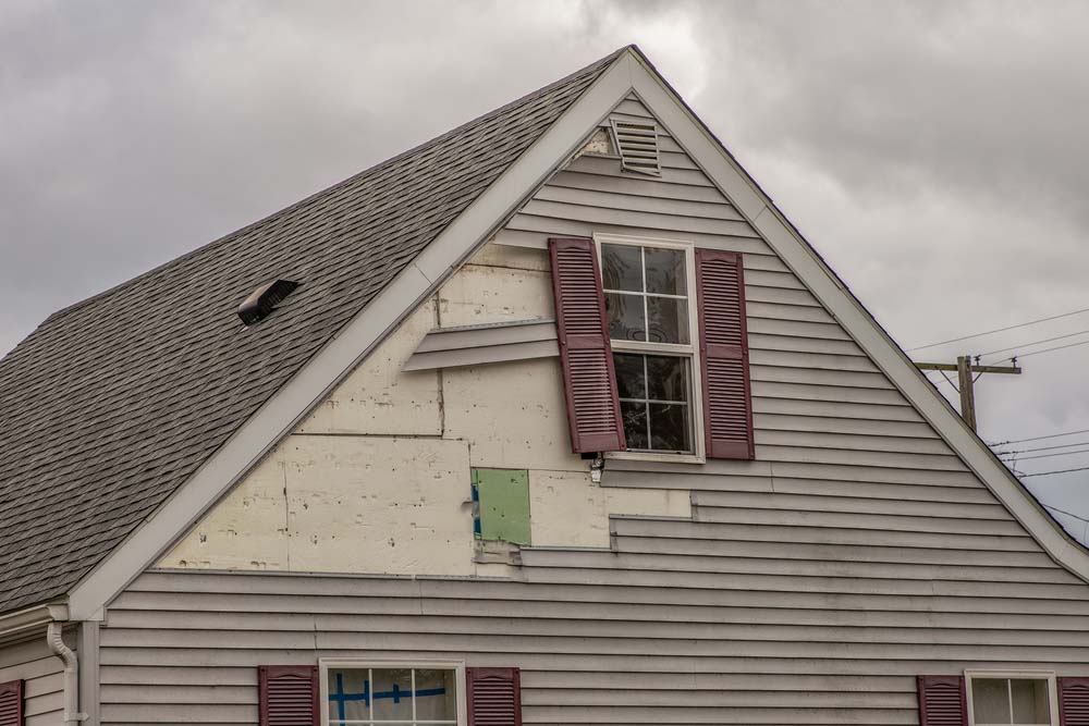 A house with siding near the roof ripped up and some dangling panels of siding.