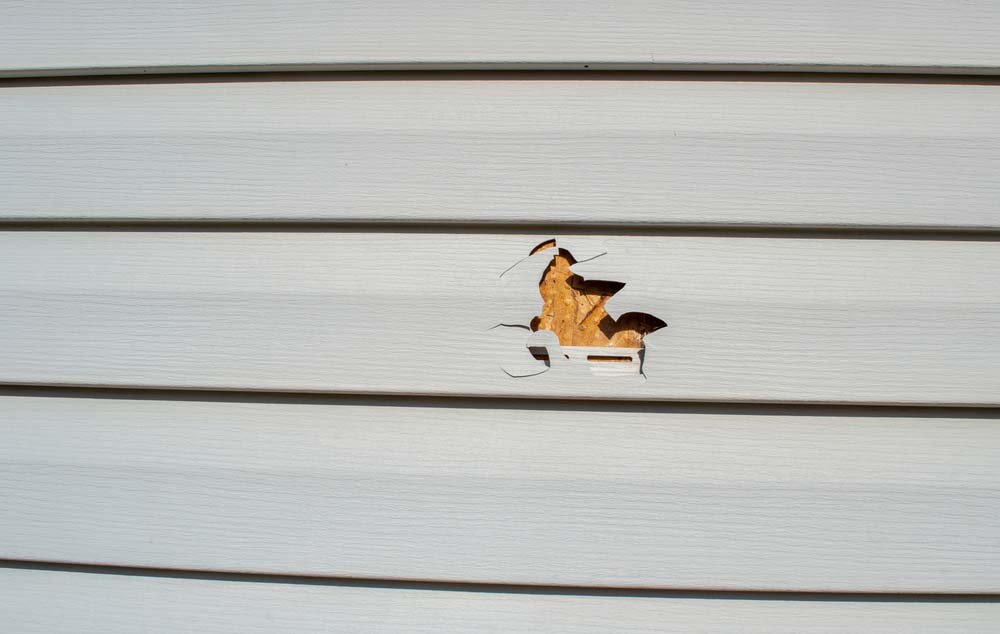 A picture of vinyl siding with a large hole punched into it.