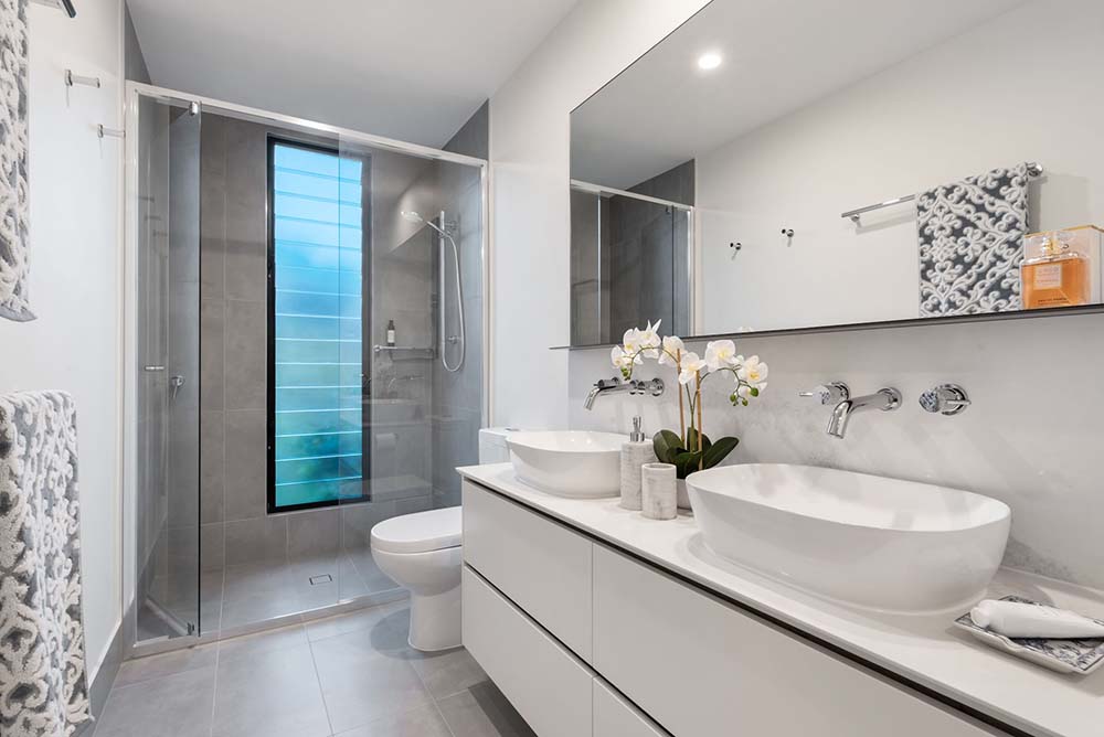 A bathroom with his and hers sinks and a stall shower with glass doors and gray tiling.