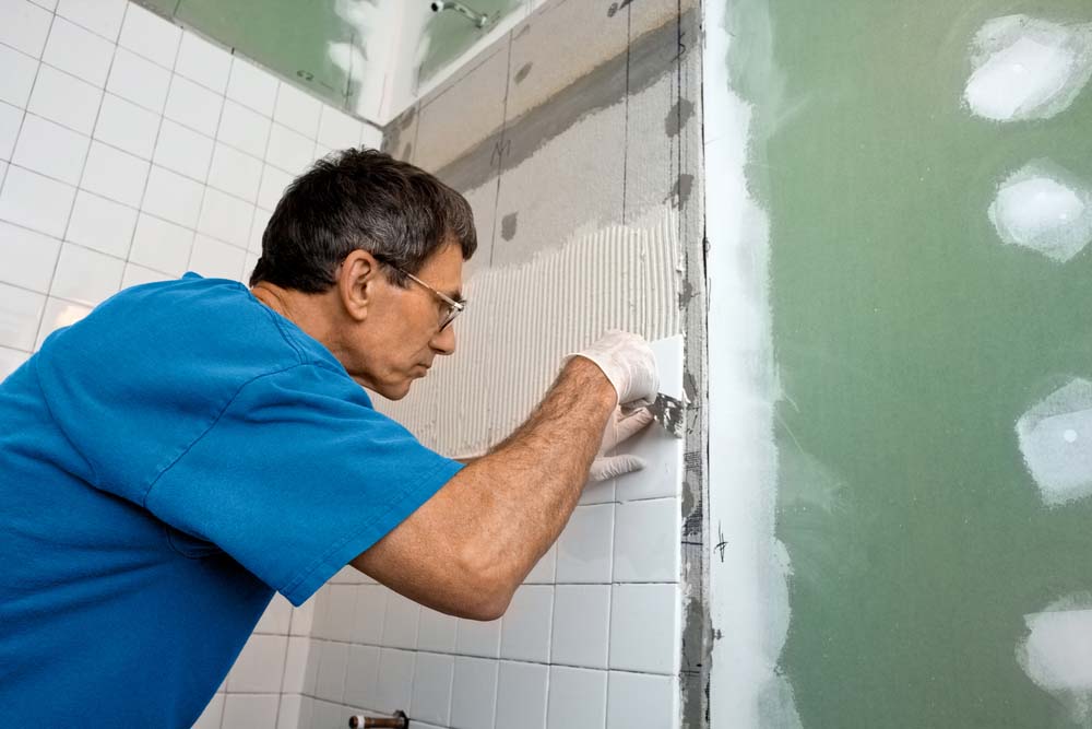A man tiles a shower wall.