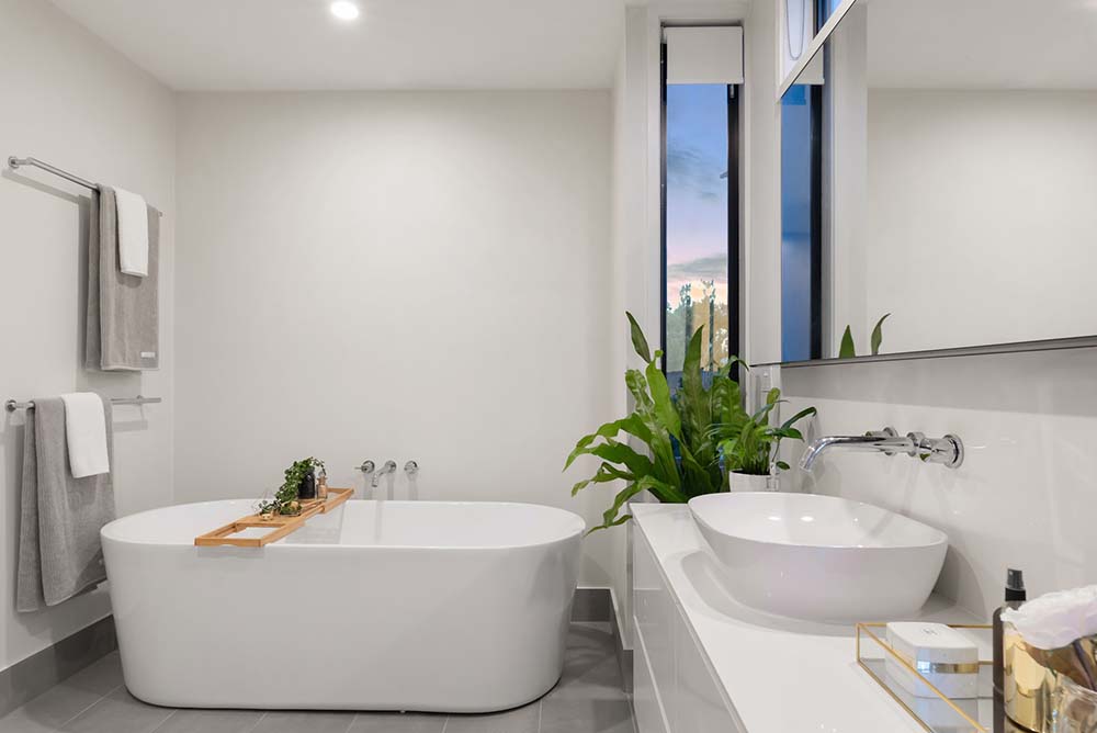 An all-white bathroom with a basin soaking tub, basin sink, and several plants.