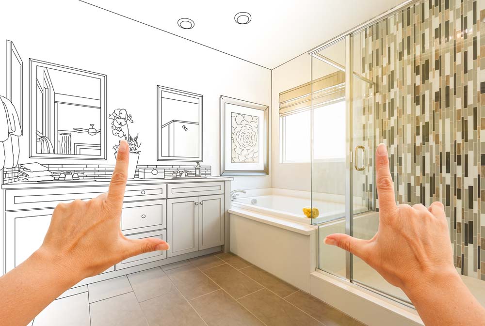 An illustration showing the plans for a bathroom next to the actual bathroom, with hands framing the image.