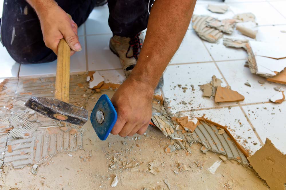 Close-up on hands using tools to remove tiling from the floor.